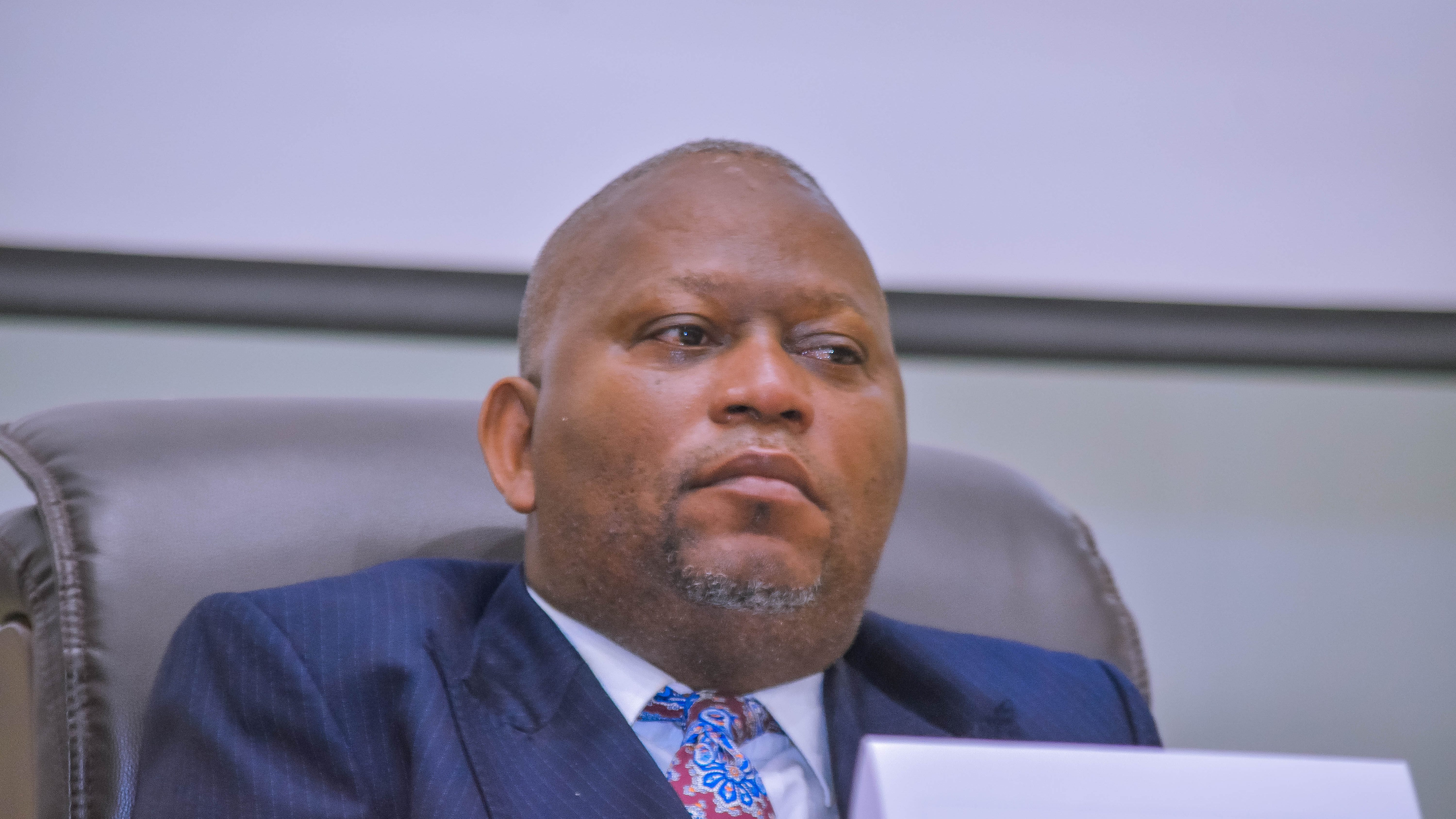 Portrait d'un homme en costume, assis et prenant la parole lors d'un événement officiel sur l'enseignement supérieur.