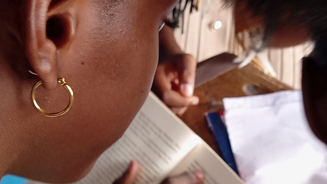 Une personne lisant un livre, se concentrant sur le texte, avec un autre individu à proximité, dans un environnement naturel.